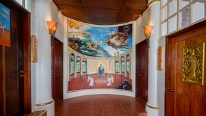 Un couloir orné d’une fresque représentant une scène religieuse, avec des portes en bois et un sol carrelé.