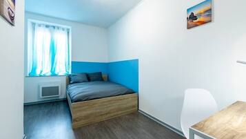 Quarto pequeno e moderno com uma cama, uma escrivaninha e uma cadeira.