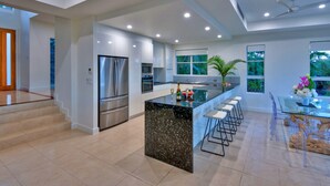 A modern kitchen with a central island, stainless steel appliances, and a glass dining area. - La Bella Waters 1 Wide Ocean Views (Whitsundays)