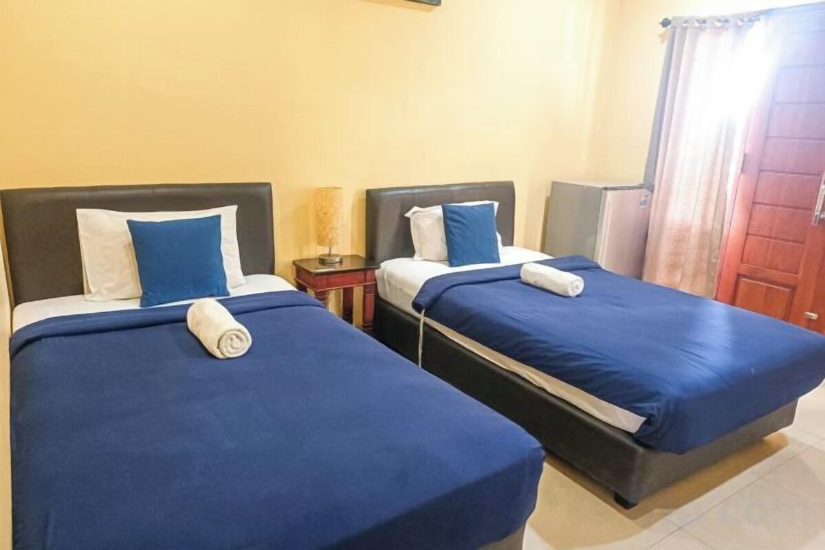 Two twin beds with blue bedding and white pillows, a nightstand with a lamp, and a wooden door with a curtain.