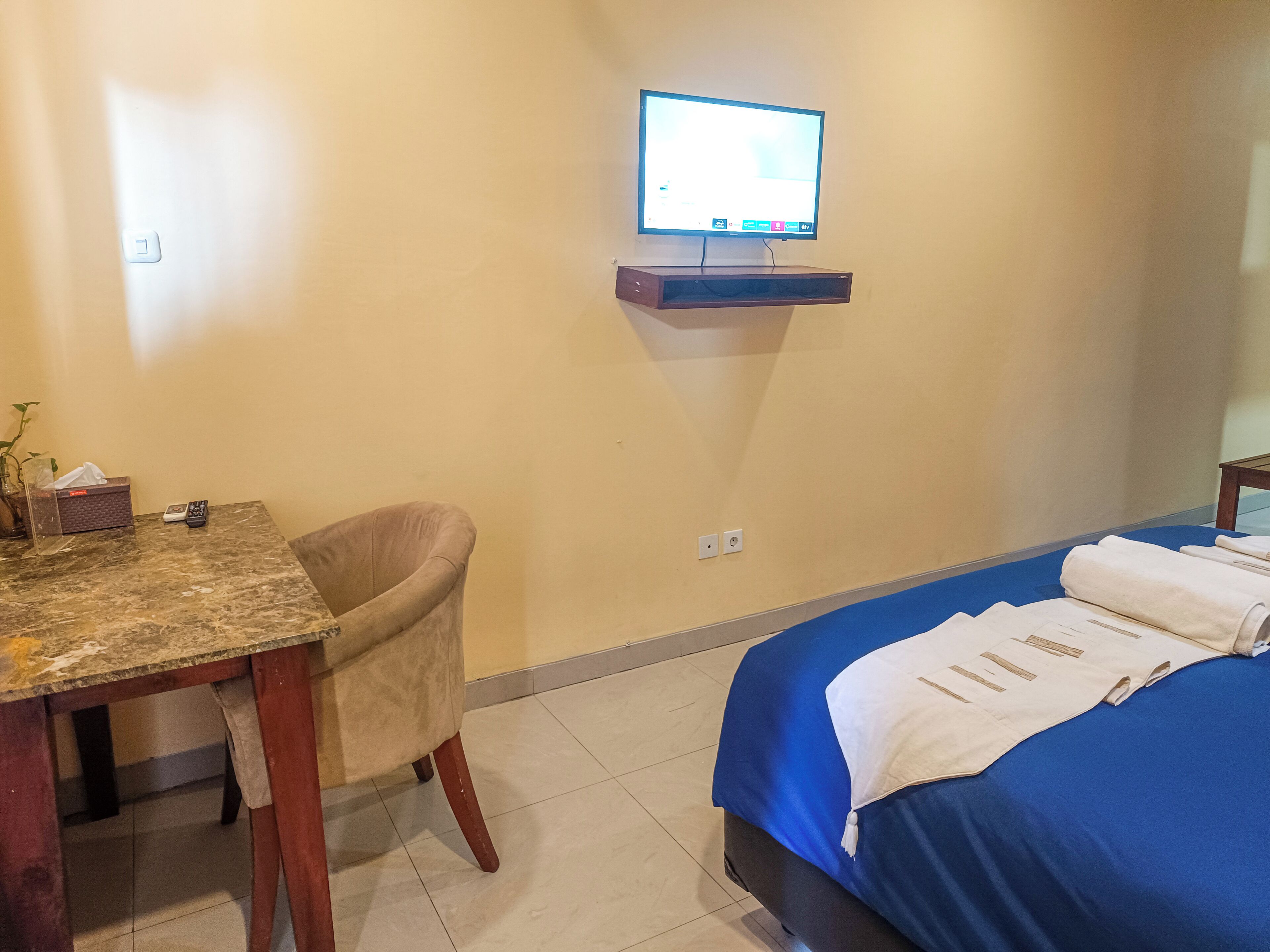 A hotel room with a bed, a desk, a chair, a television on a shelf, and a bathroom with a towel rack.