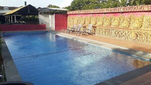 A swimming pool with a red wall and decorative carvings, surrounded by lounge chairs. - Kuta Paradise 777 (Legian)
