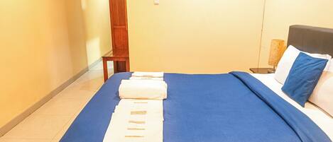 A hotel room with a neatly made bed, a wooden nightstand, a lamp, and a painting on the wall.