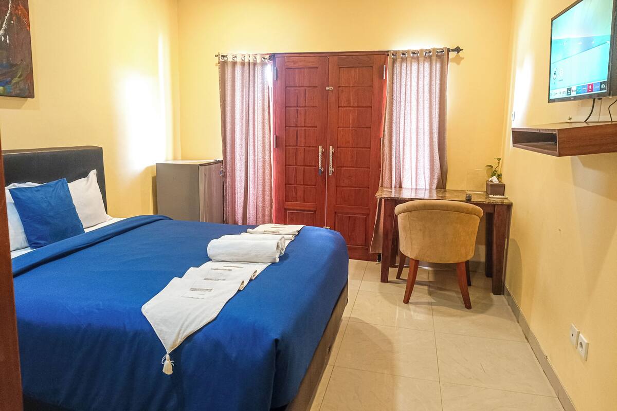 A hotel room with a bed, a desk, a chair, a TV, and a wardrobe.