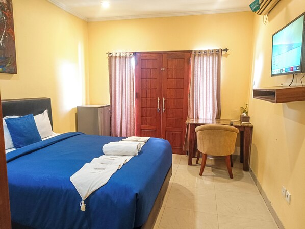 A hotel room with a bed, a desk, a chair, a TV, and a wardrobe.