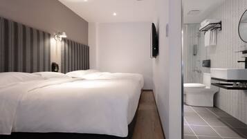Una habitación de hotel moderna con una cama grande, una mesita de noche, un televisor de pantalla plana y un baño con inodoro, lavamanos y espejo.