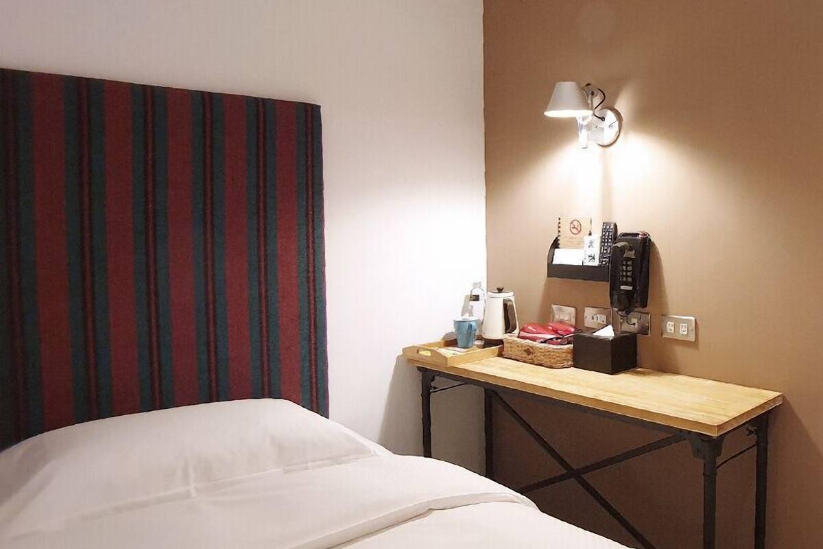 Quarto de hotel com uma cama, uma mesa de cabeceira com abajur, telefone e carregador de parede.