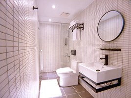 Un bagno moderno con doccia rivestita in piastrelle bianche, un water e un lavandino con specchio sopra.