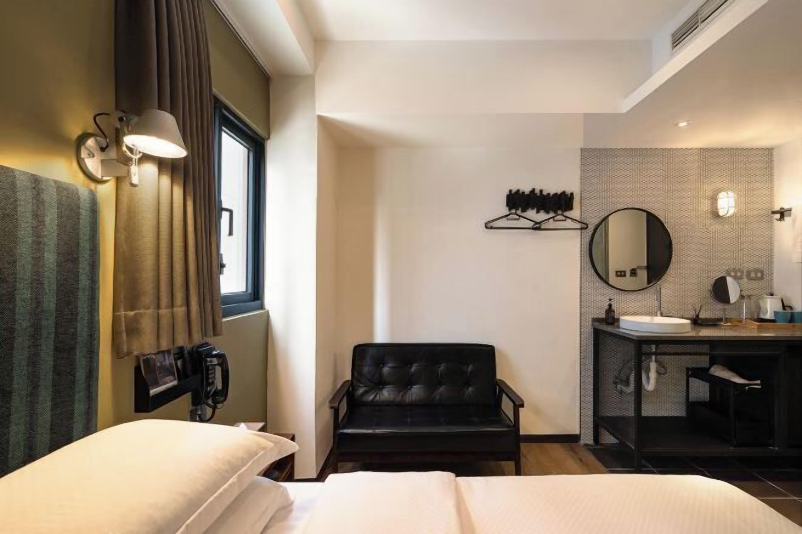 Ein Hotelzimmer mit Bett, Stuhl, Schreibtisch mit Spiegel und einem Fenster mit Vorhängen.