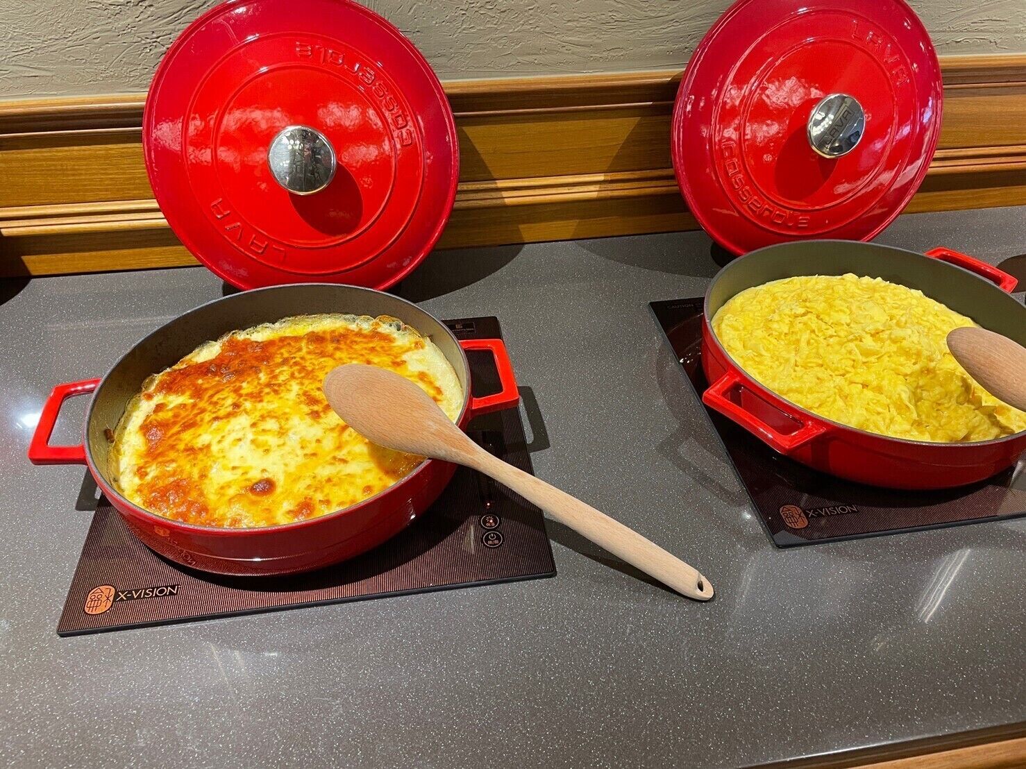 Two red pots on a stove with lids, one containing scrambled eggs and the other a baked dish.