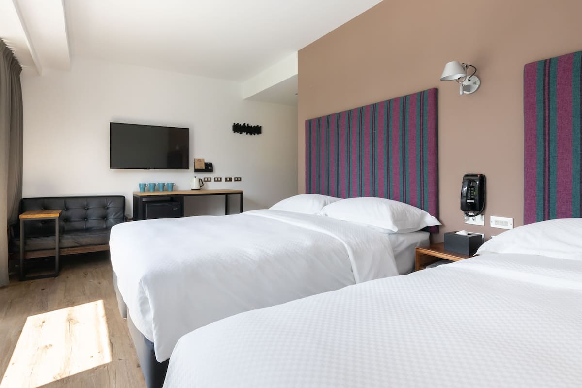 Quarto de hotel com duas camas, televisão de tela plana, escrivaninha com abajur e telefone.