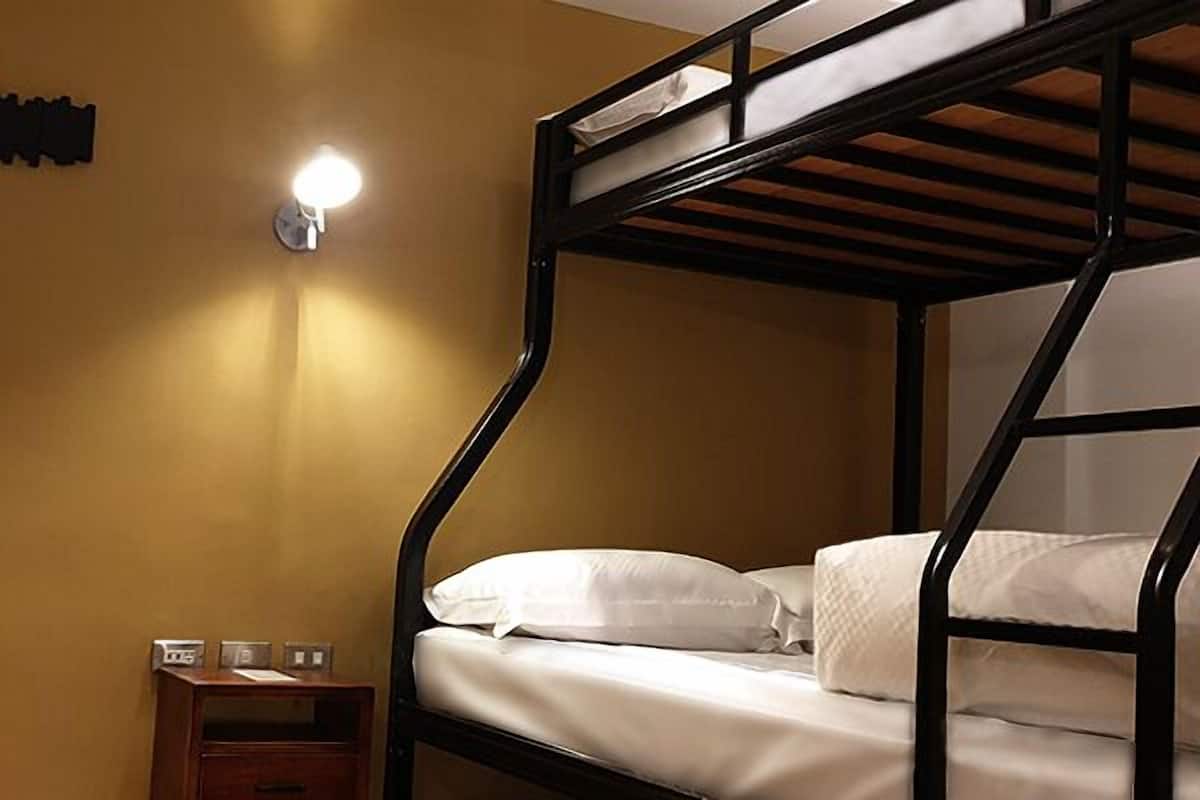 Quarto com beliche, luminária fixada na parede e uma pequena mesa de cabeceira de madeira com relógio.