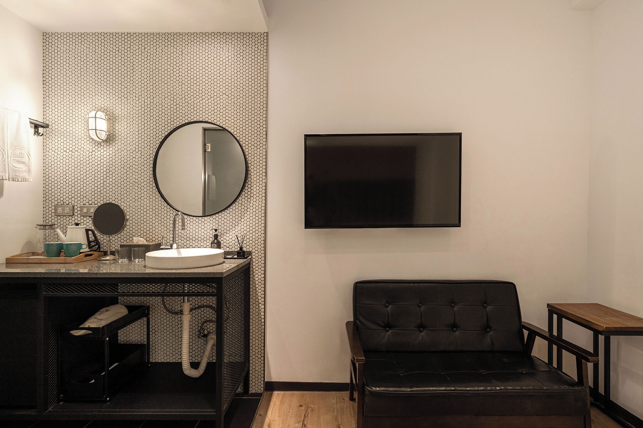 A modern bathroom with a round mirror, a sink, a toilet, and a flat-screen TV mounted on the wall.