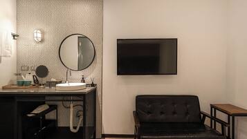 A modern bathroom with a round mirror, a sink, a toilet, and a flat-screen TV mounted on the wall.