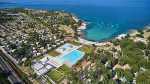 Vista aérea de un complejo turístico frente al mar con una gran piscina, playa y numerosas cabañas junto a la playa.