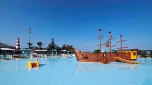 Una piscina con una estructura de barco de madera, sillas de descanso y un faro al fondo.