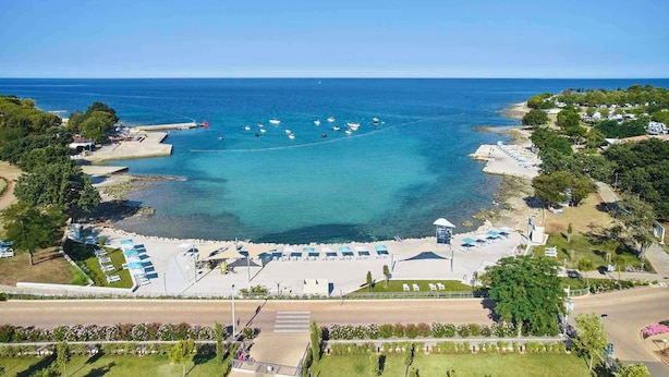 Vista aérea de una zona costera con playa, barcos y un estacionamiento con sombrillas.