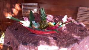 Una mesa con un mantel estampado, una cesta roja tejida que contiene una piña, flores y otros objetos.
