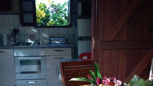 Una cocina con ventana, una mesa de comedor con mantel tropical y una silla de madera.