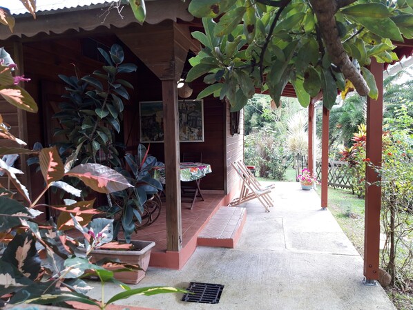 Un espace extérieur abrité, agrémenté de plantes en pot, d’une table avec des chaises et d’un chemin menant à un jardin.