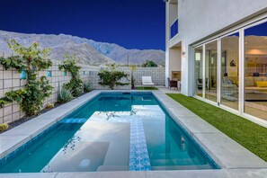 A swimming pool with a view of mountains, a covered patio, and a modern house with sliding glass doors.