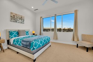A bedroom with a large bed, a view of a cityscape, and a ceiling fan.