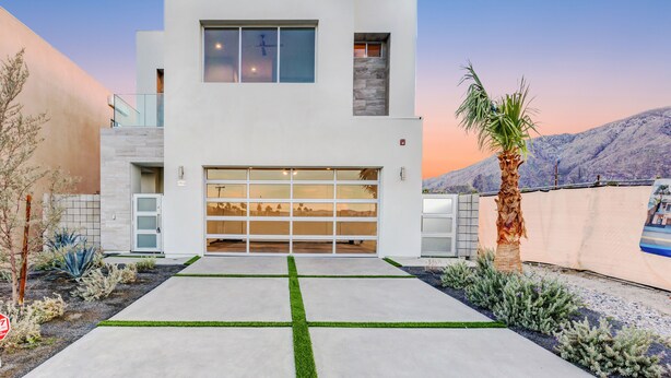 A modern two-story house with a large garage, a cross-shaped driveway, and a mountain backdrop. - Mountain View Luxury Resort-Style Modern Home with a Private Pool. (Palm Springs)