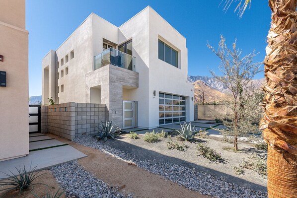 A modern two-story house with a garage, a balcony, and a desert garden.