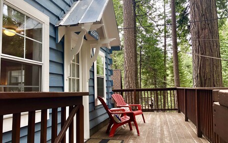 A wooden deck with a railing, two red Adirondack chairs, and a house with blue siding and a white porch.