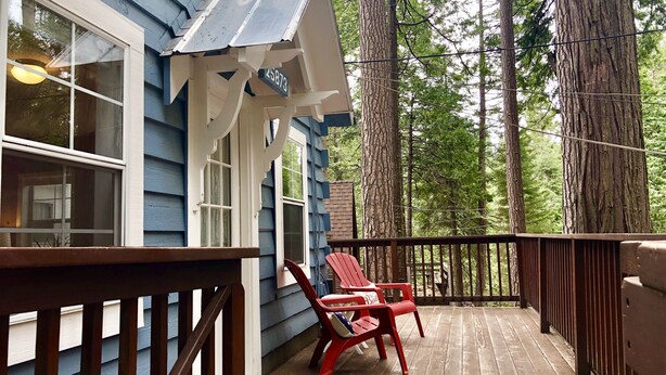 En træterrasse med gelænder, to røde Adirondack-stole og et hus med blåsider og en hvid veranda.