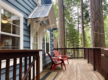 A wooden deck with a railing, two red Adirondack chairs, and a house with blue siding and a white porch.