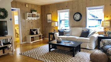 A cozy living room with a white sofa, a coffee table, a patterned rug, and a clock on the wall.