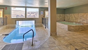 An indoor swimming pool with a view of a cityscape through large windows, a separate hot tub area, and a tiled floor. - Lovely Studio with Pond and Mountain Views! (Granby)
