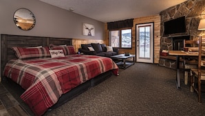 A cozy room with a large bed, a sofa, a coffee table, and a fireplace. - Lovely Studio with Pond and Mountain Views! (Granby)