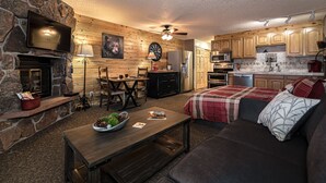 A cozy living room with a fireplace, wooden walls, a TV, and a dining area. - Lovely Studio with Pond and Mountain Views! (Granby)