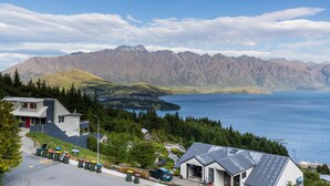 A mountain view with a lake, a building with a garage, and a parking area with trash bins.