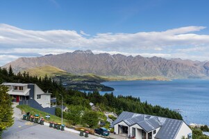 A mountain view with a lake, a building with a garage, and a parking area with trash bins.