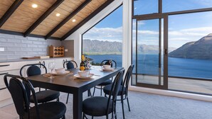 A dining area with a view of a lake and mountains, featuring a wooden ceiling, black chairs, and a table set with plates, glasses, and a bottle.