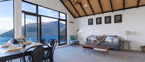 A dining area with a view of the sea and mountains, a sofa, and a lamp.