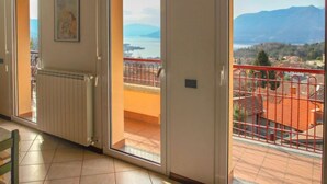 A room with a view of a lake and mountains, a radiator, and a door leading to an outdoor balcony with a red railing. - Achillea by Interhome (Luino)