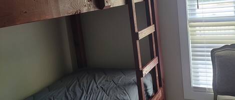 Una cama litera con escalera, una silla y una ventana con persianas.