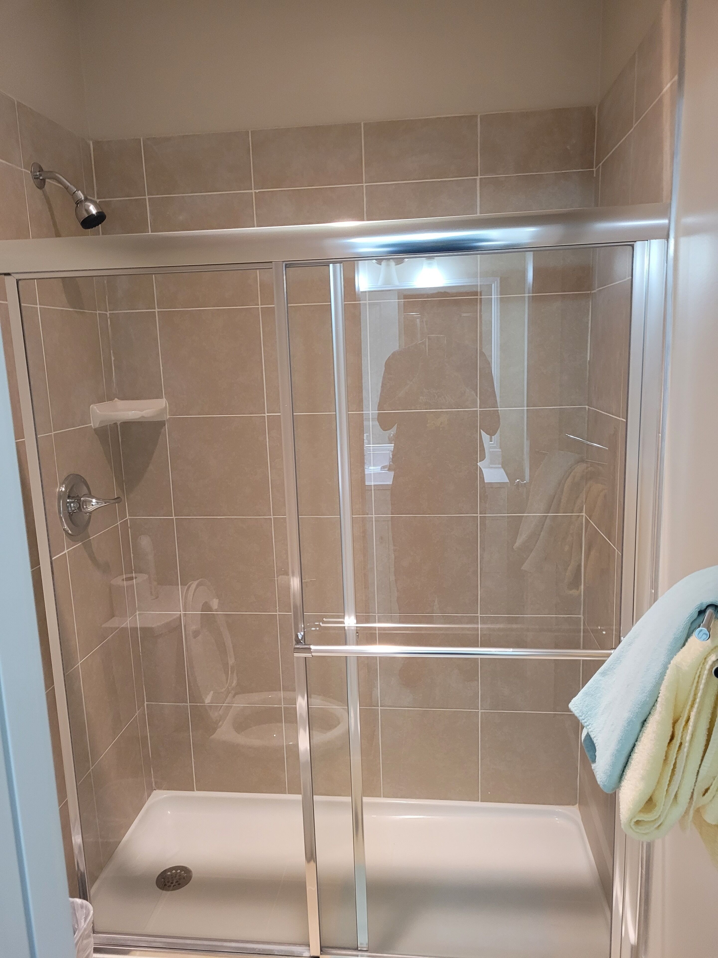 Cabina de ducha con paredes de vidrio, cabezal de ducha manual, puerta de cristal y un perchero con toallas.