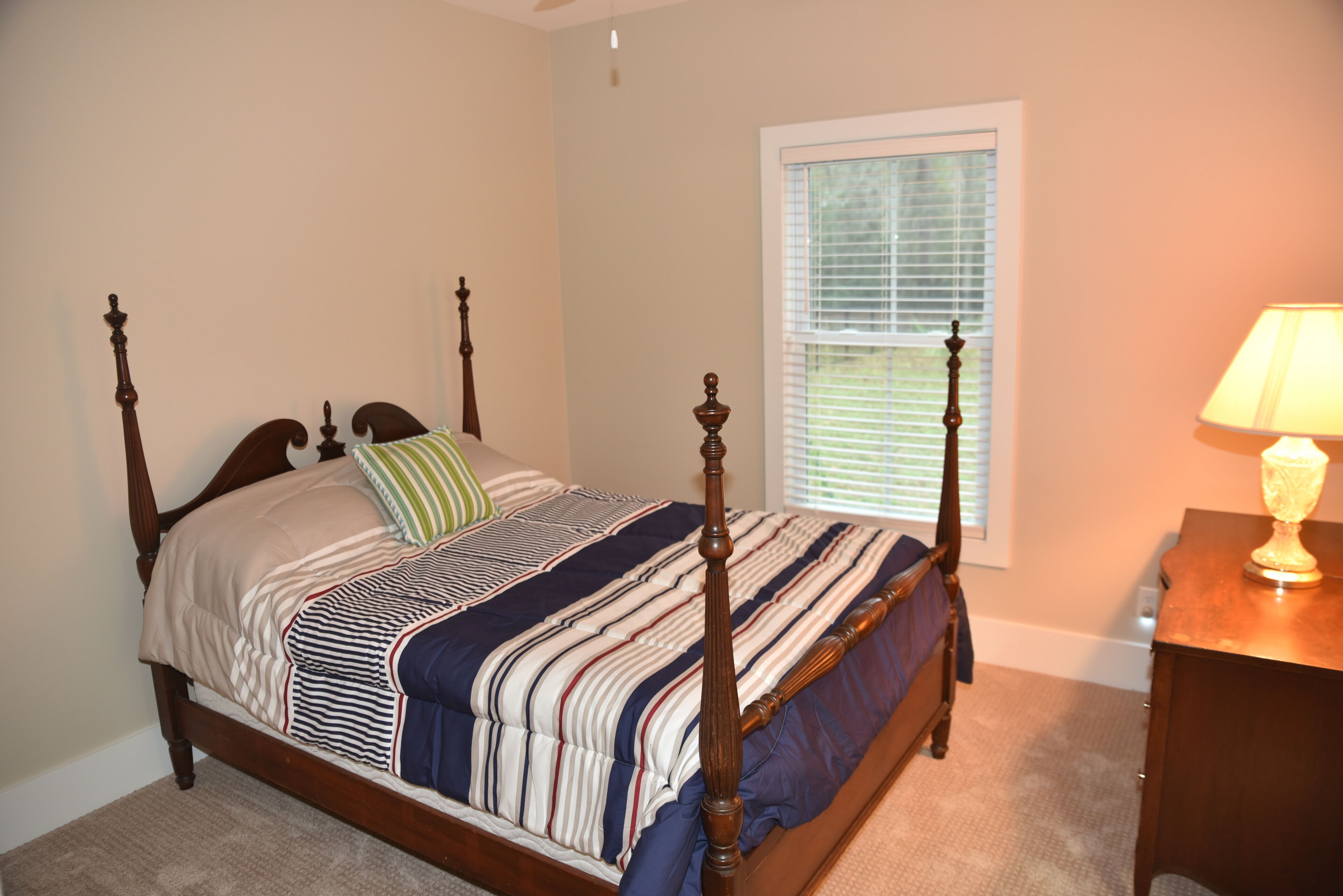 A four-poster bed with a striped bedspread, a green pillow, and a wooden nightstand with a lamp.