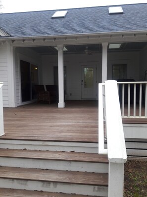 A covered porch with a wooden deck, white railings, and a door leading to an interior room.