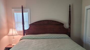 A bedroom with a four-poster bed, a ceiling fan, a bedside lamp, and a window with blinds.