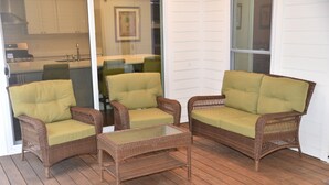 A wicker furniture set with cushions on a wooden deck, a glass door leading to a kitchen, and a white exterior wall. - Ranch, 6 bedrooms and 5 baths home near Parris Island and Beaufort is beautiful. (St Helena Island)