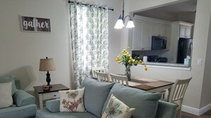 Una sala de estar con sofá, una mesita, una lámpara y un comedor con sillas y un florero.