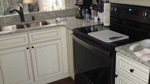 Una cocina con armarios blancos, un microondas negro, una estufa y un fregadero.