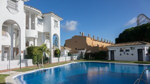 En swimmingpool med ett klart, blått vatten, omgiven av en vit byggnad med valv och en beige byggnad med ett tak belagt med tegelpannor i bakgrunden.
