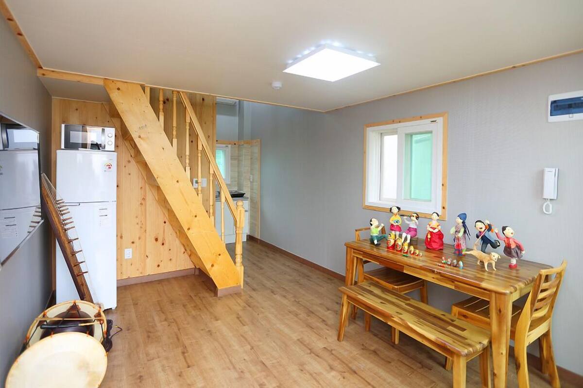 Una cocina compacta con una escalera de madera, una mesa de comedor con sillas y un refrigerador.
